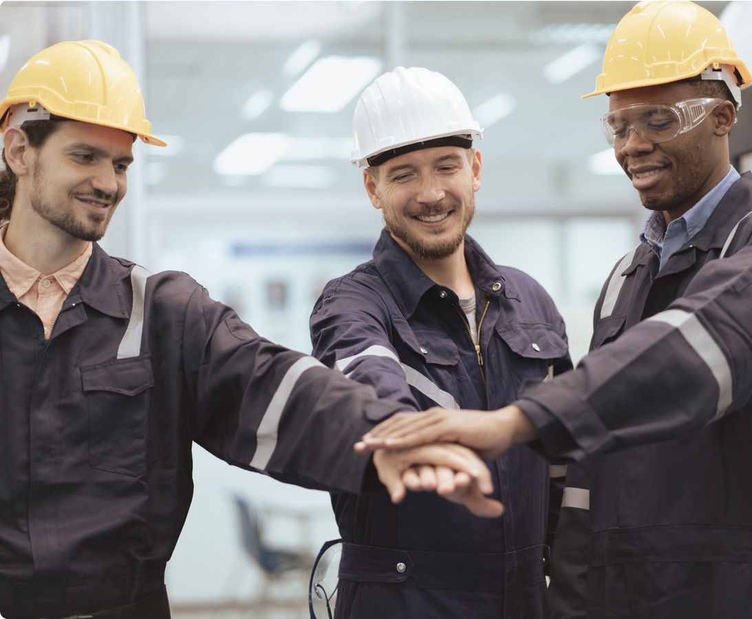 Drei Männer in Schutzhelmen und Overalls stehen vereint, was die Bedeutung von Teamarbeit und Kooperation verdeutlicht